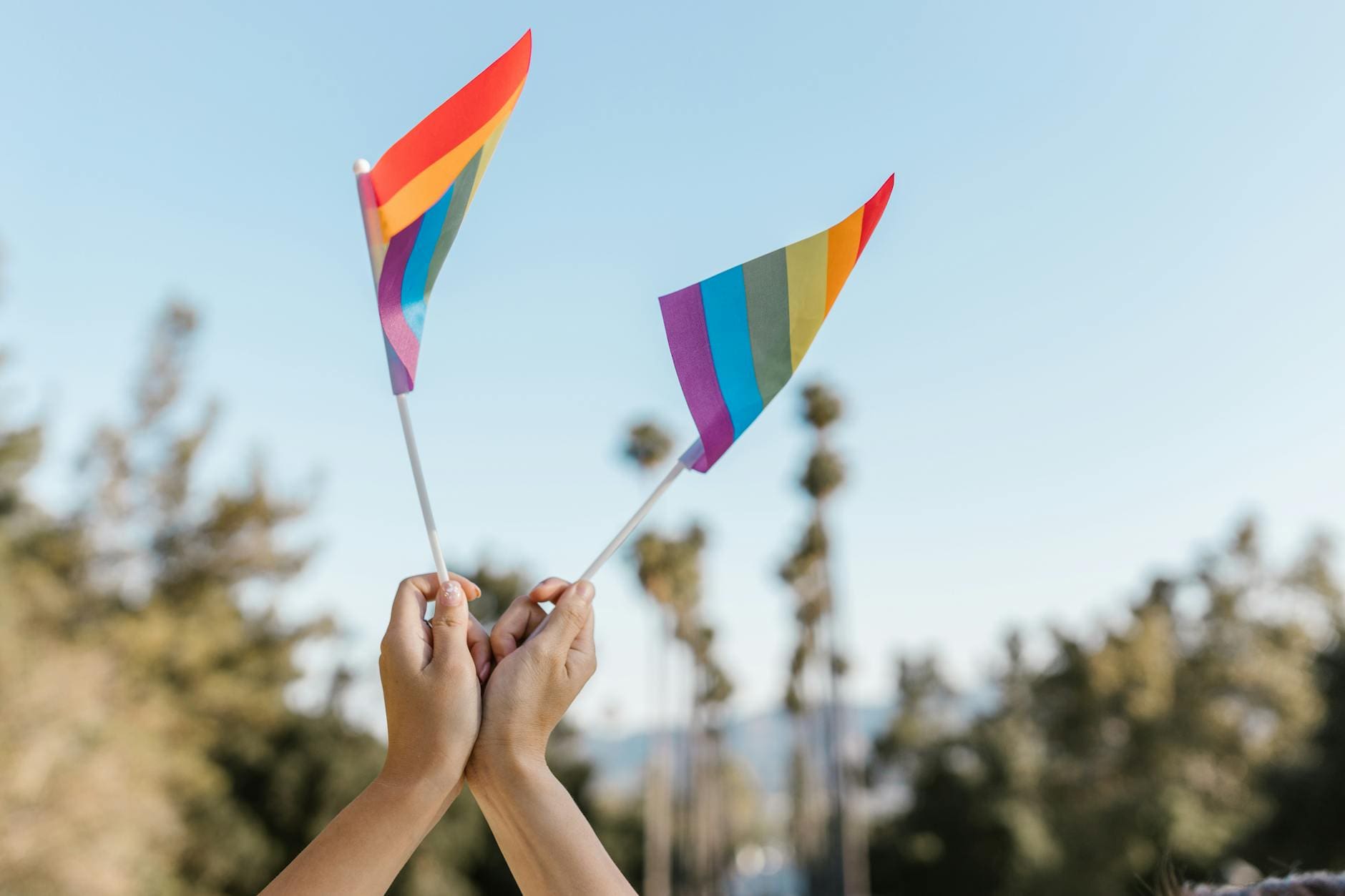 two unrecognizable hands holding high small rainbow flags